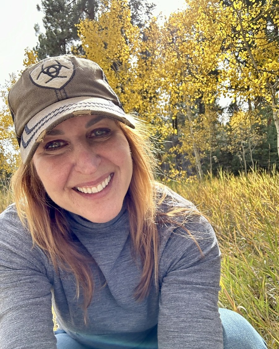 Marylou, founder of Built With You, smiling outdoors in a ball cap with golden aspen trees behind her